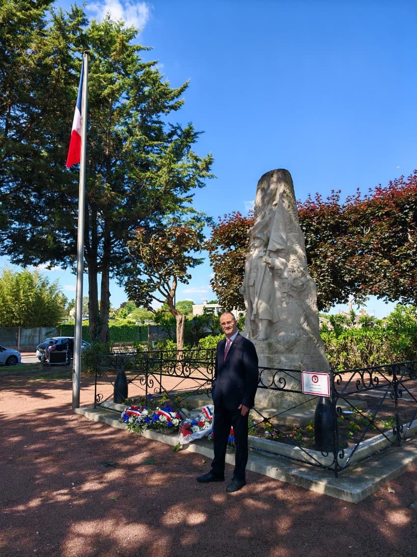 Jean-Noël Sanchez devant le monument aux morts, drapeau tricolore et gerbes au pied de la stèle.