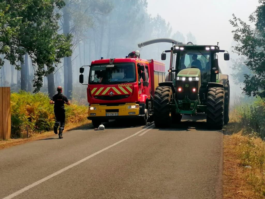 Camion de pompiers et tracteur agricole sur une route, dans la fumée d'un feu de forêt en Gironde.